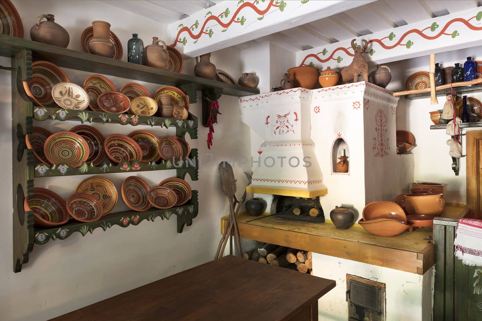 Ceramic painted bowls, plates and jugs on a wooden shelf on the wall, an old oven with a glassware in the interior of the ancient Ukrainian rural house.