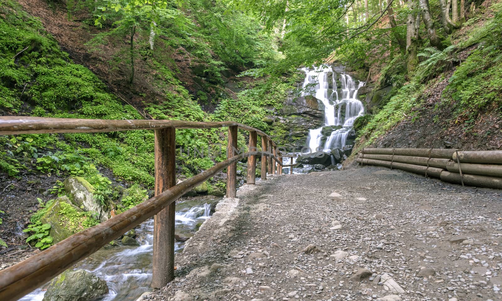 A well-groomed path to the waterfall along the fast mountain river between the hills of the Carpathian Mountains.