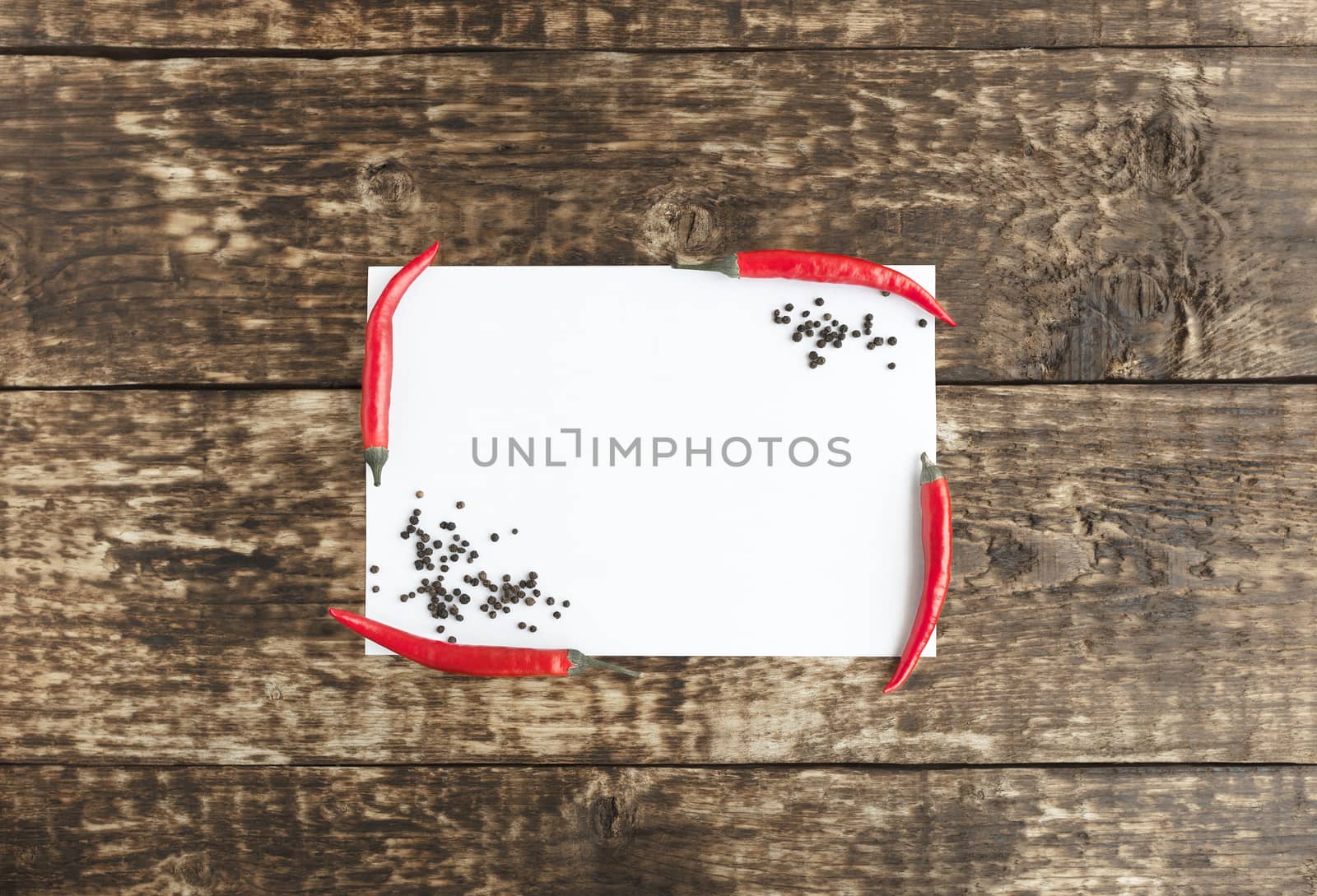 Red hot chili peppers on old wooden table with white sheet of paper for text