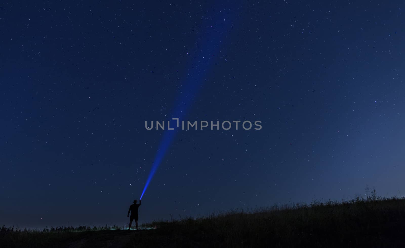 Silhouette of man on a background of stars he directs a ray of light onto a dark blue starry sky