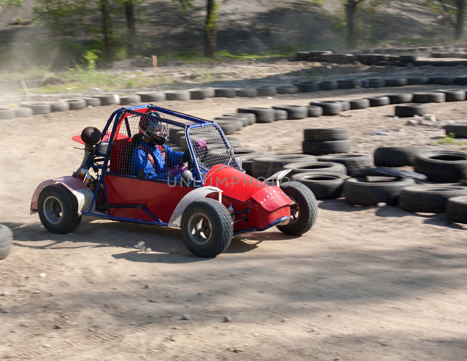 Race of a teenager on a children's buggy kicking up trail of dust on sand track