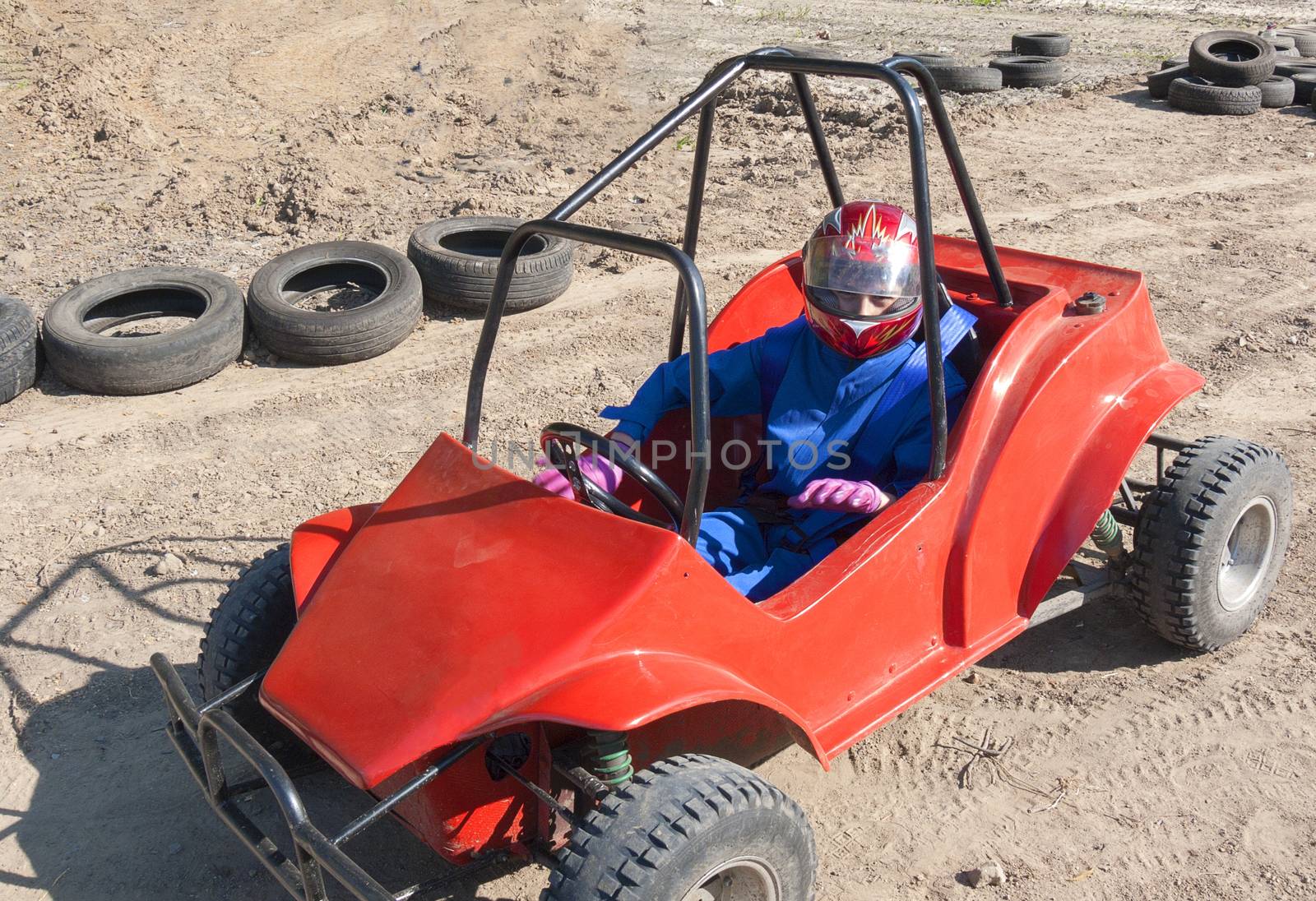 Race of a teenager on a children's buggy kicking up trail of dust on sand track