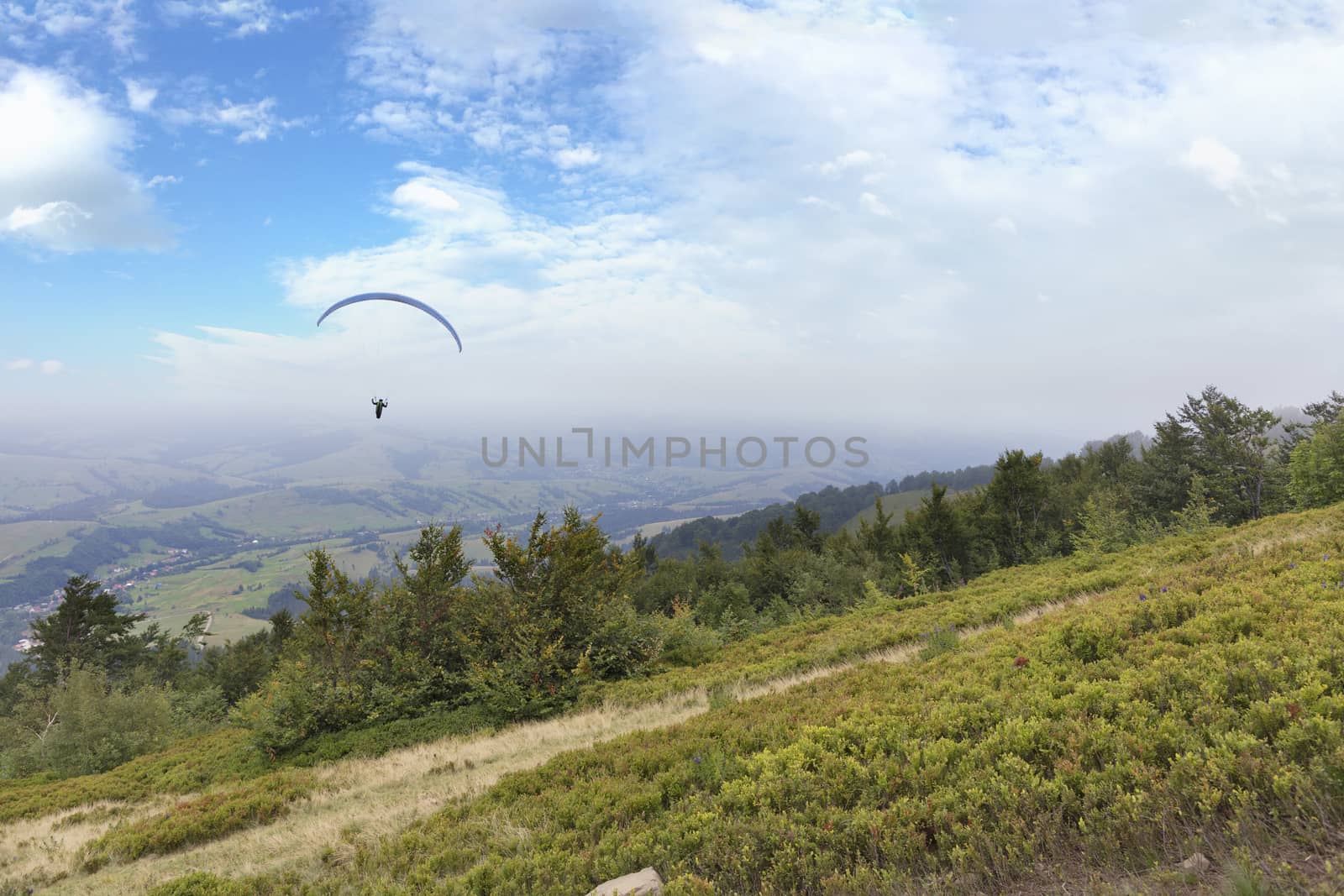 A flying paraglider against the blue sky, in the morning fog of the Carpathian Mountains