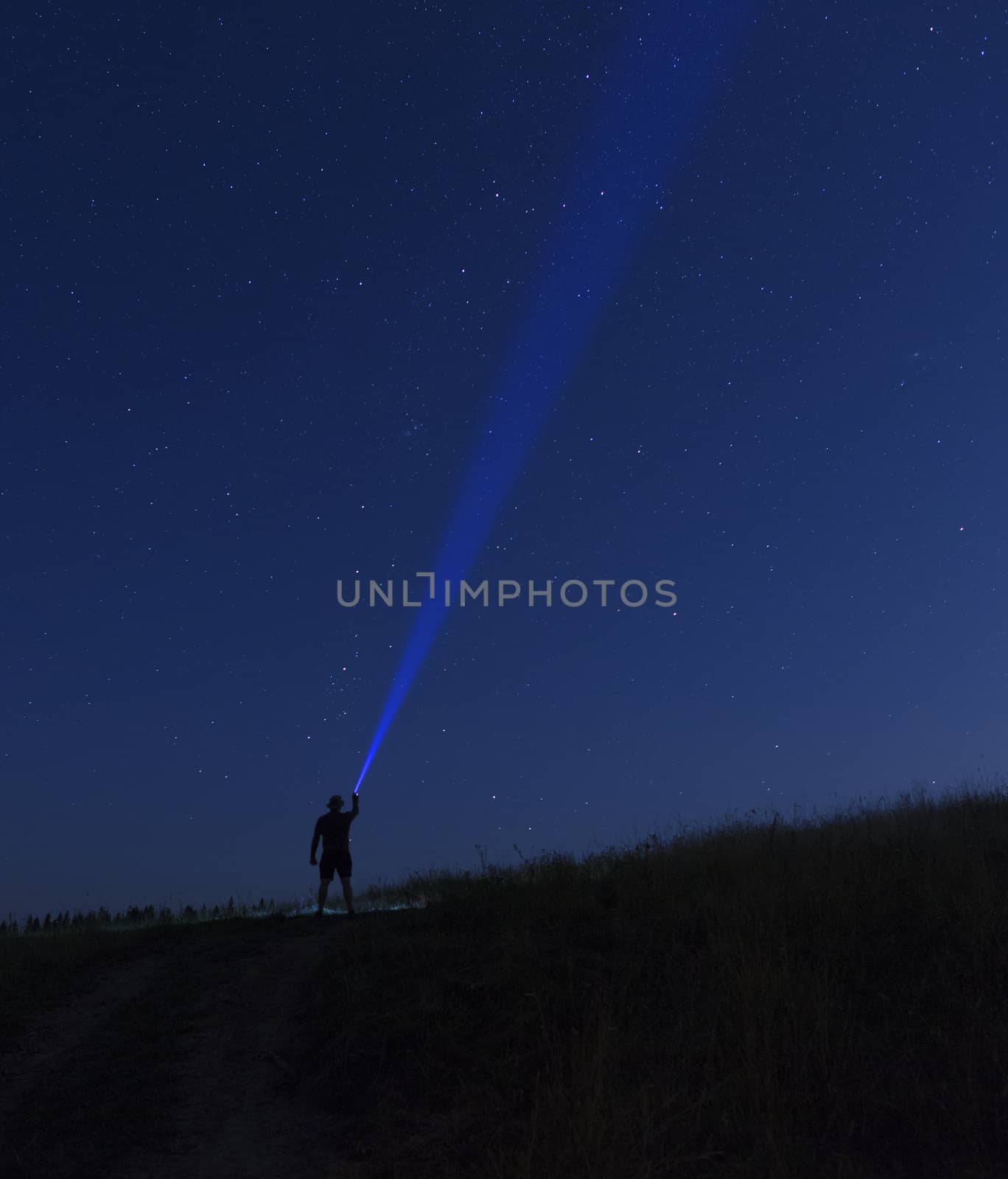 Silhouette of man on a background of stars he directs a ray of light onto a dark blue starry sky