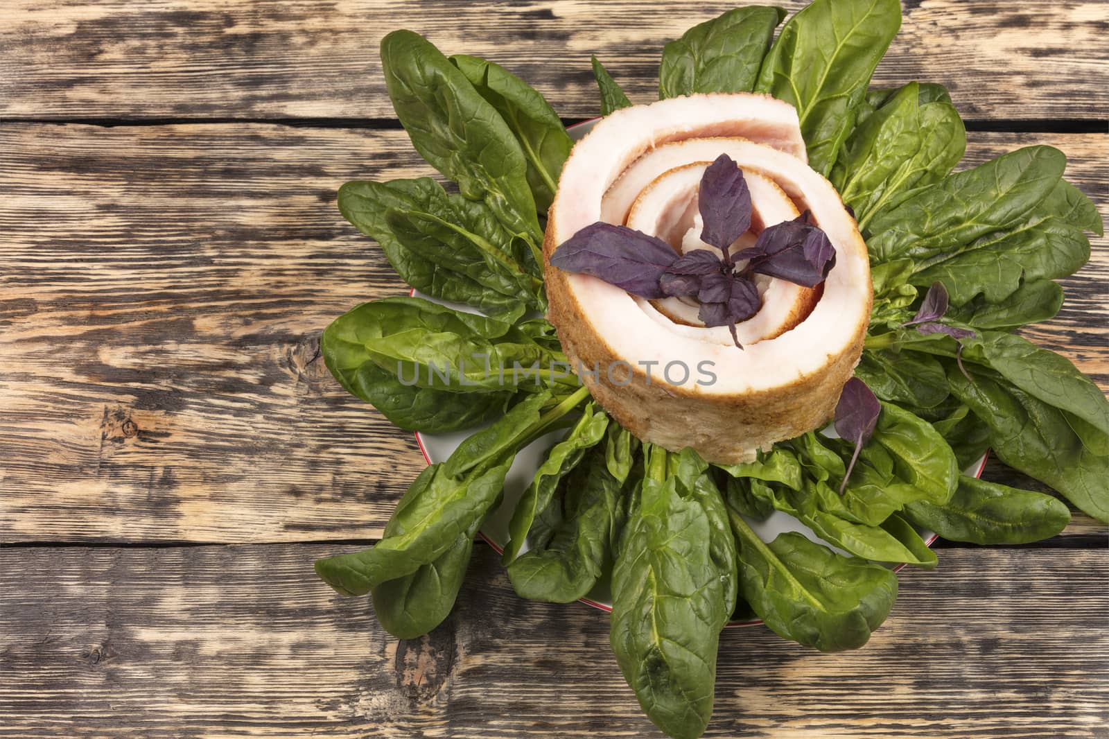 A beautiful slice of fresh bacon with spinach and basil leaves on a porcelain white plate on the background of an old weathered wooden surface