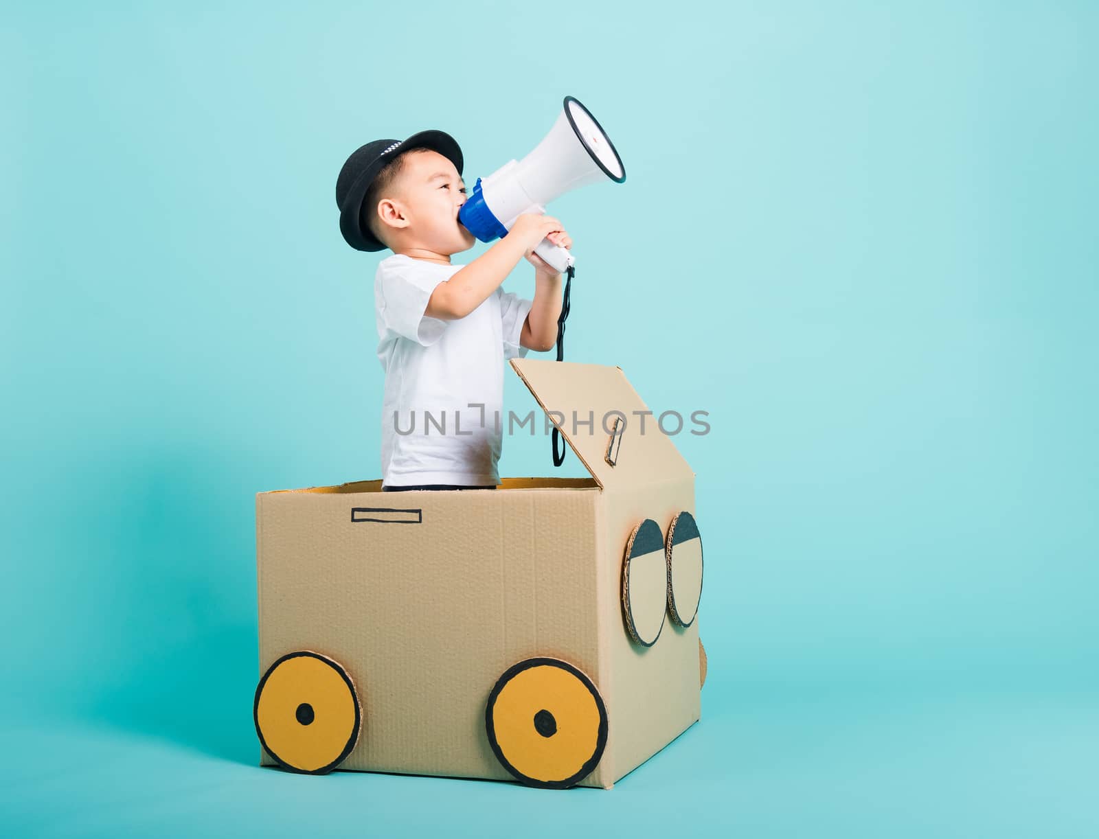 Happy Asian children boy smile in driving play car creative by a cardboard box imagination with megaphone, summer holiday travel concept, studio shot on blue background with copy space for text