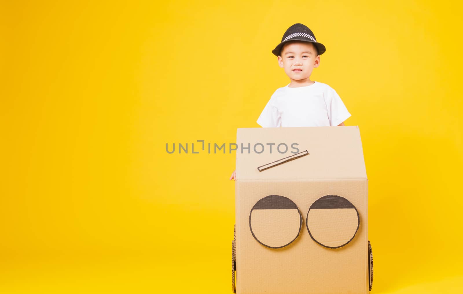 Portrait happy Asian cute little children boy smile so happy wearing white T-shirt driving car creative by cardboard, studio shot on yellow background with copy space