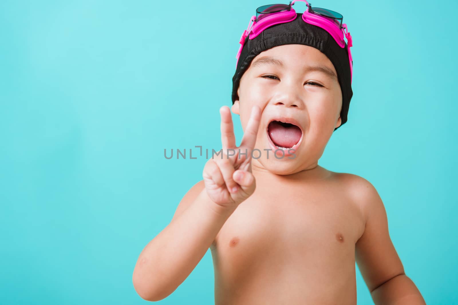 Summer vacation concept, Closeup portrait Asian happy cute little child boy wearing goggles and swimsuit, Kid having fun with in summer vacation looking camera, studio shot isolated blue background