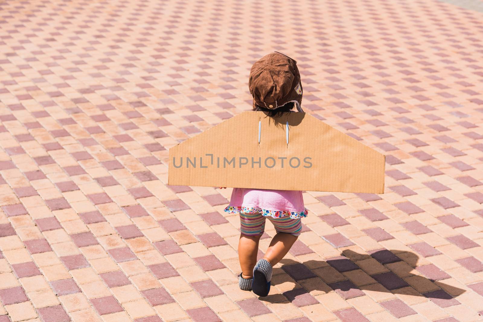 Happy Asian funny child or kid little girl smile wear pilot hat and goggles play toy cardboard airplane wing flying against summer sky cloud on trees garden background, Startup freedom concept