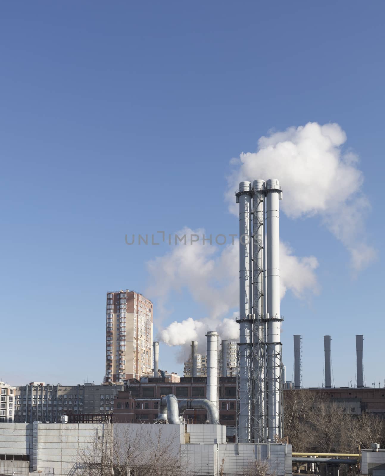 White smoke comes from a white chimney heat station pipe on a blue sky background. The environment. Greenhouse effect.