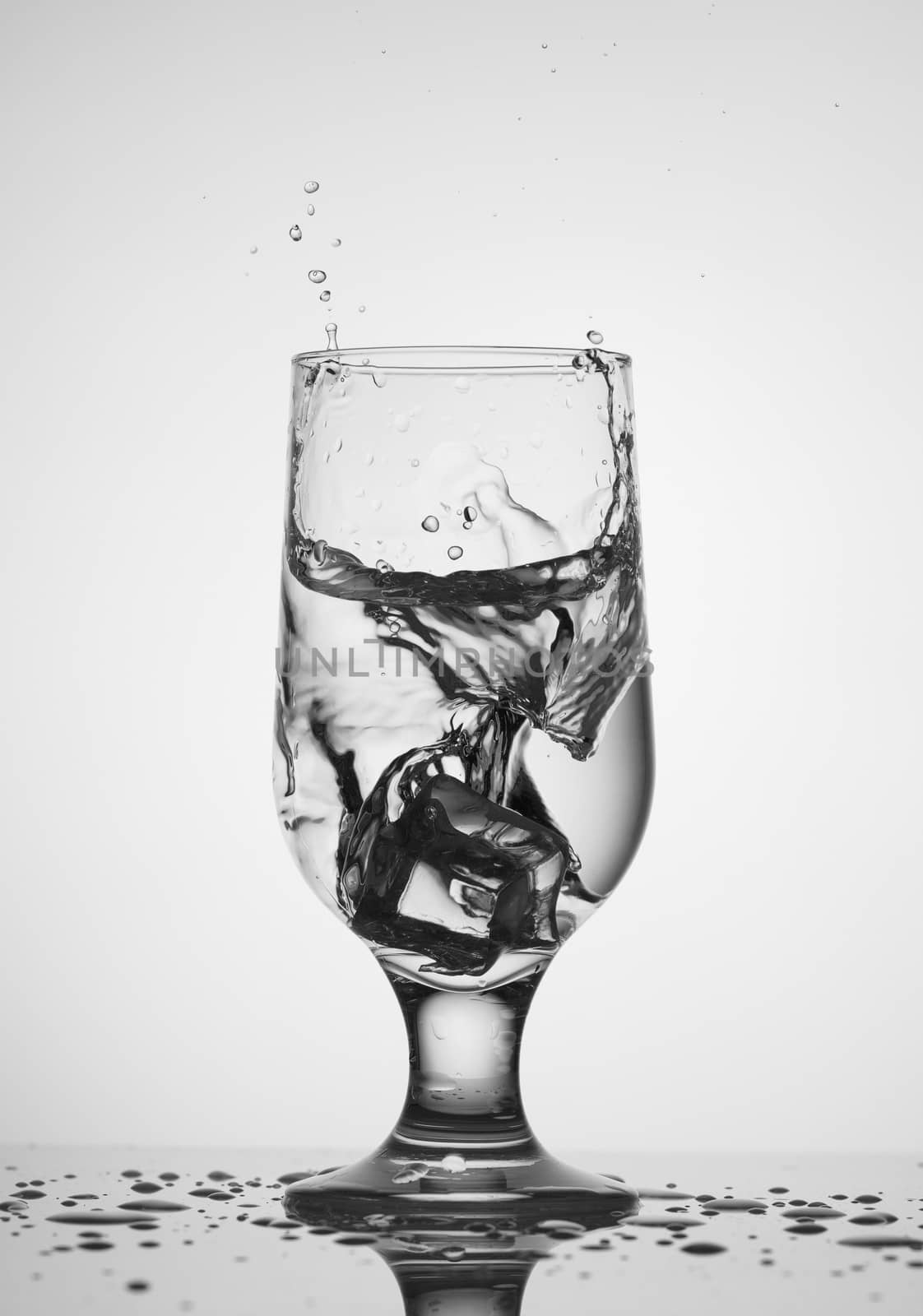 An ice cube falls into a glass glass with water by Sergii