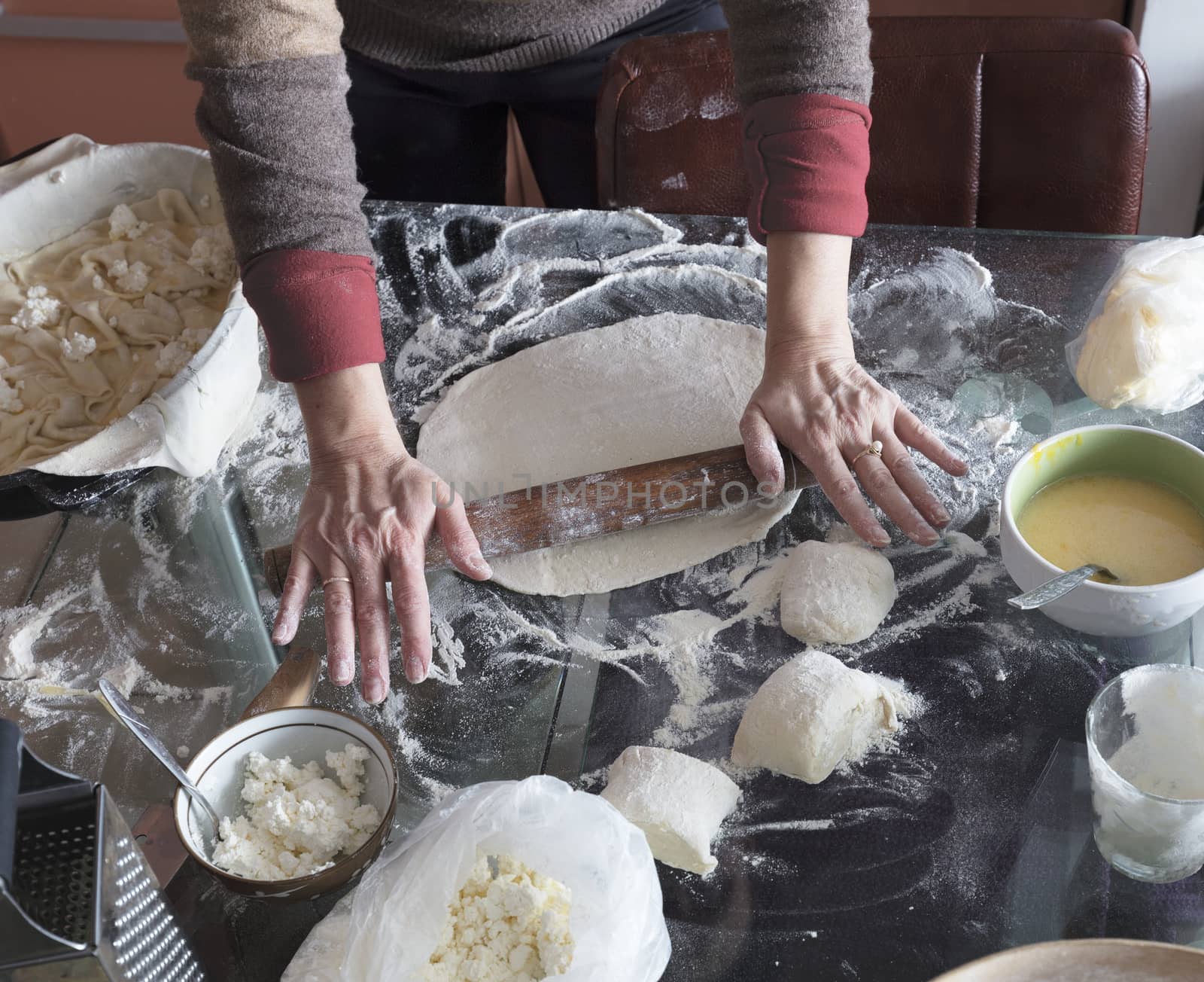 Female hands roll the dough on a glass table to make a cake with cottage cheese.