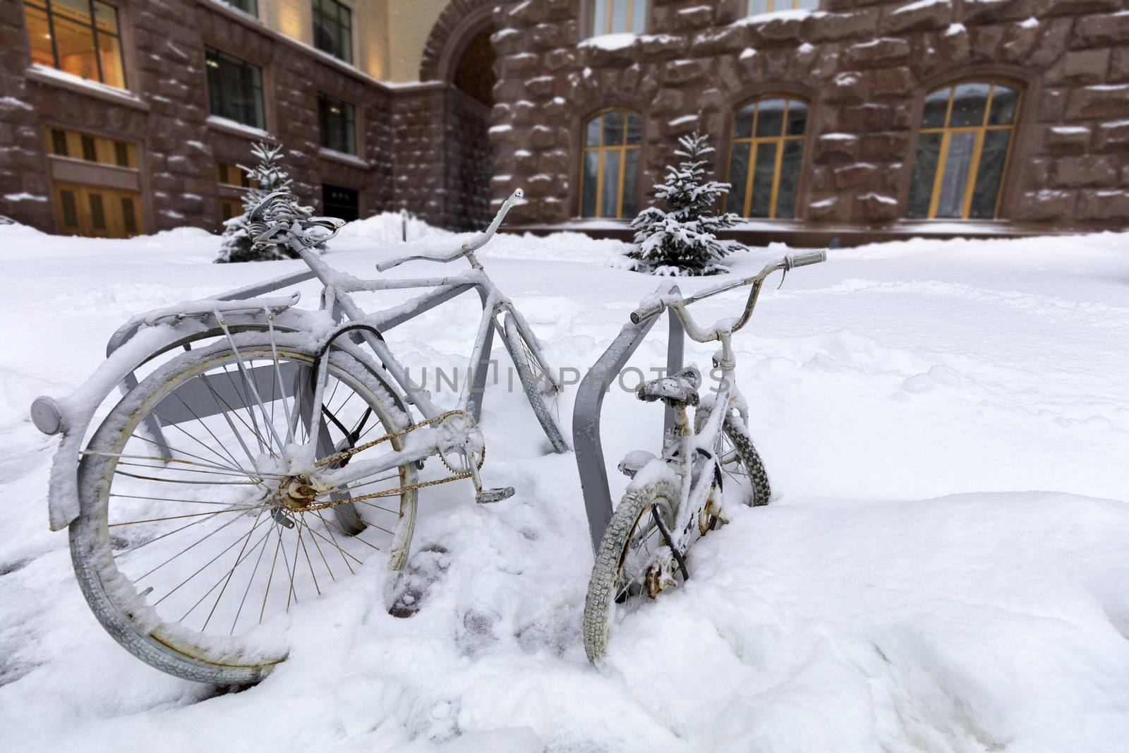 Two bicycles chained to a rack outside are covered in snow during a snowfall by Sergii