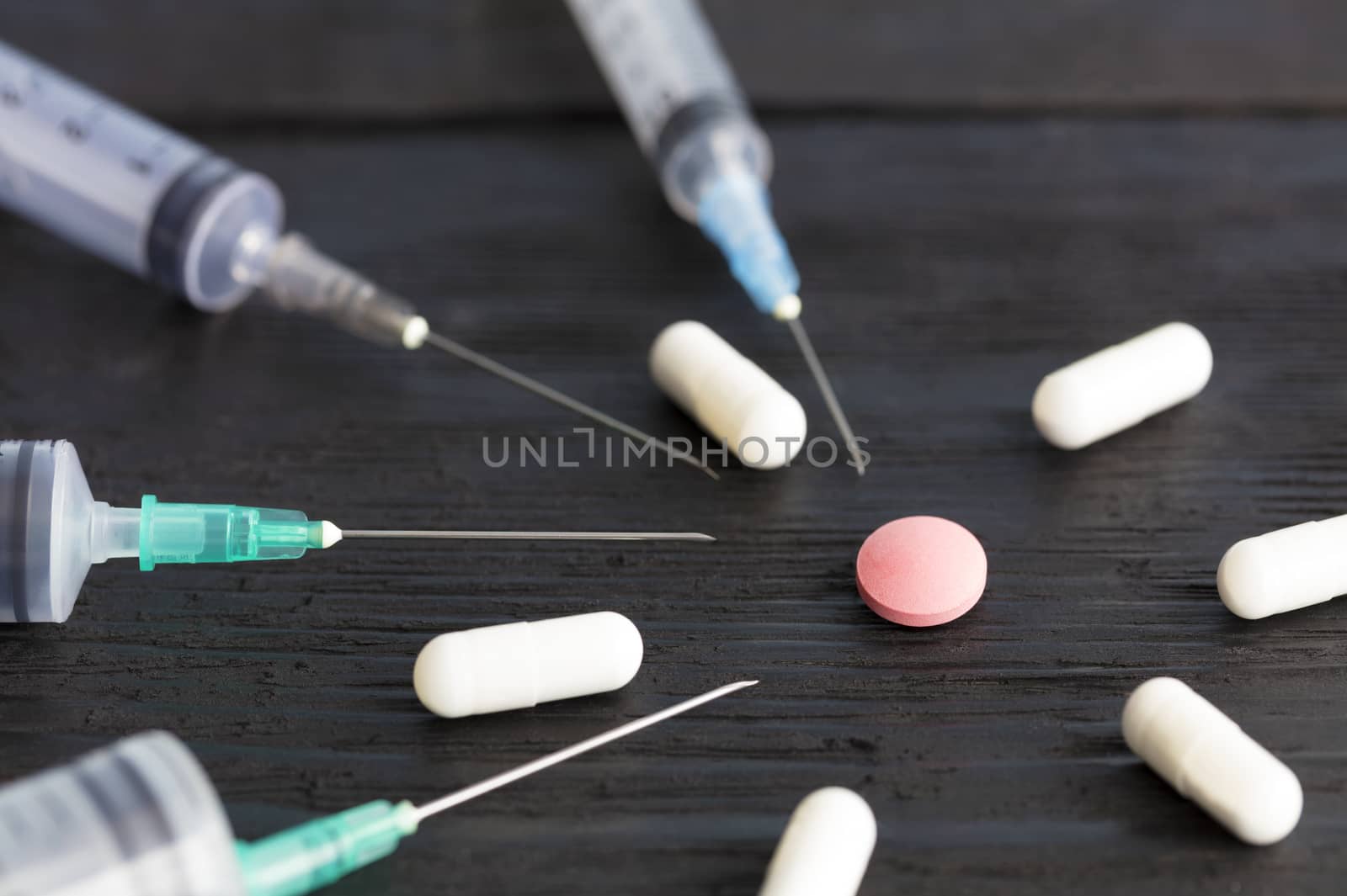 Medical syringes of various capacities, capsules, tablets lie on an old black wooden board and point to a red round tablet.