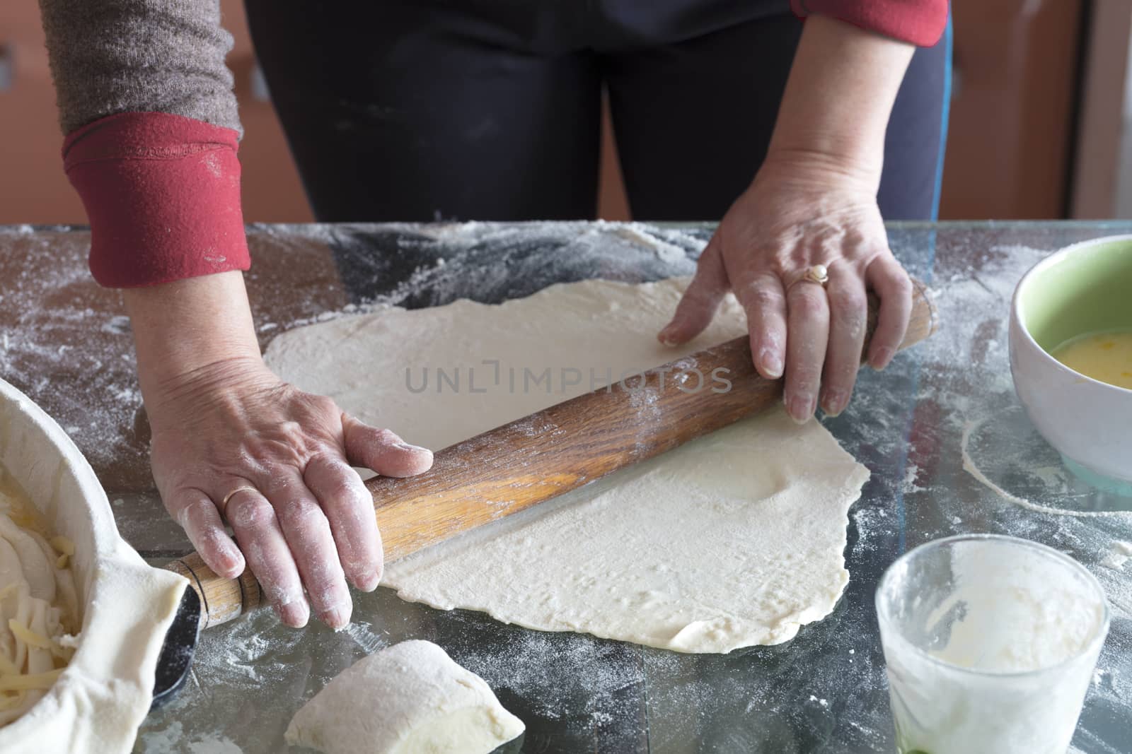 Female hands roll the dough on a glass table to make a cake with cottage cheese.