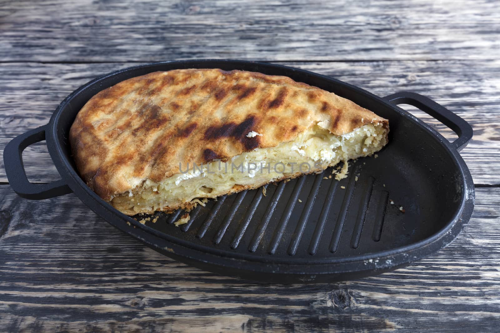 Homemade cake with cottage cheese and Parmesan cheese, which melted in a hot oven. Pie on a cast iron plate on an old wooden background.
