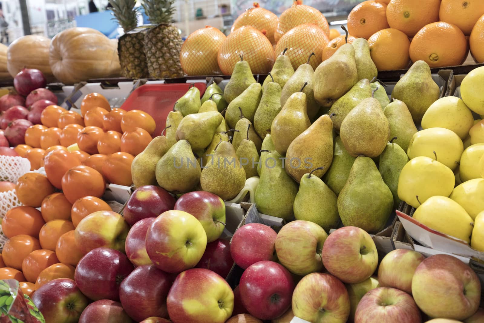 Bright background of fresh fruits. Oranges, apples, pears, pineapple, pomegranate, pumpkin, persimmonlie lie in the trays in the market and attract attention.