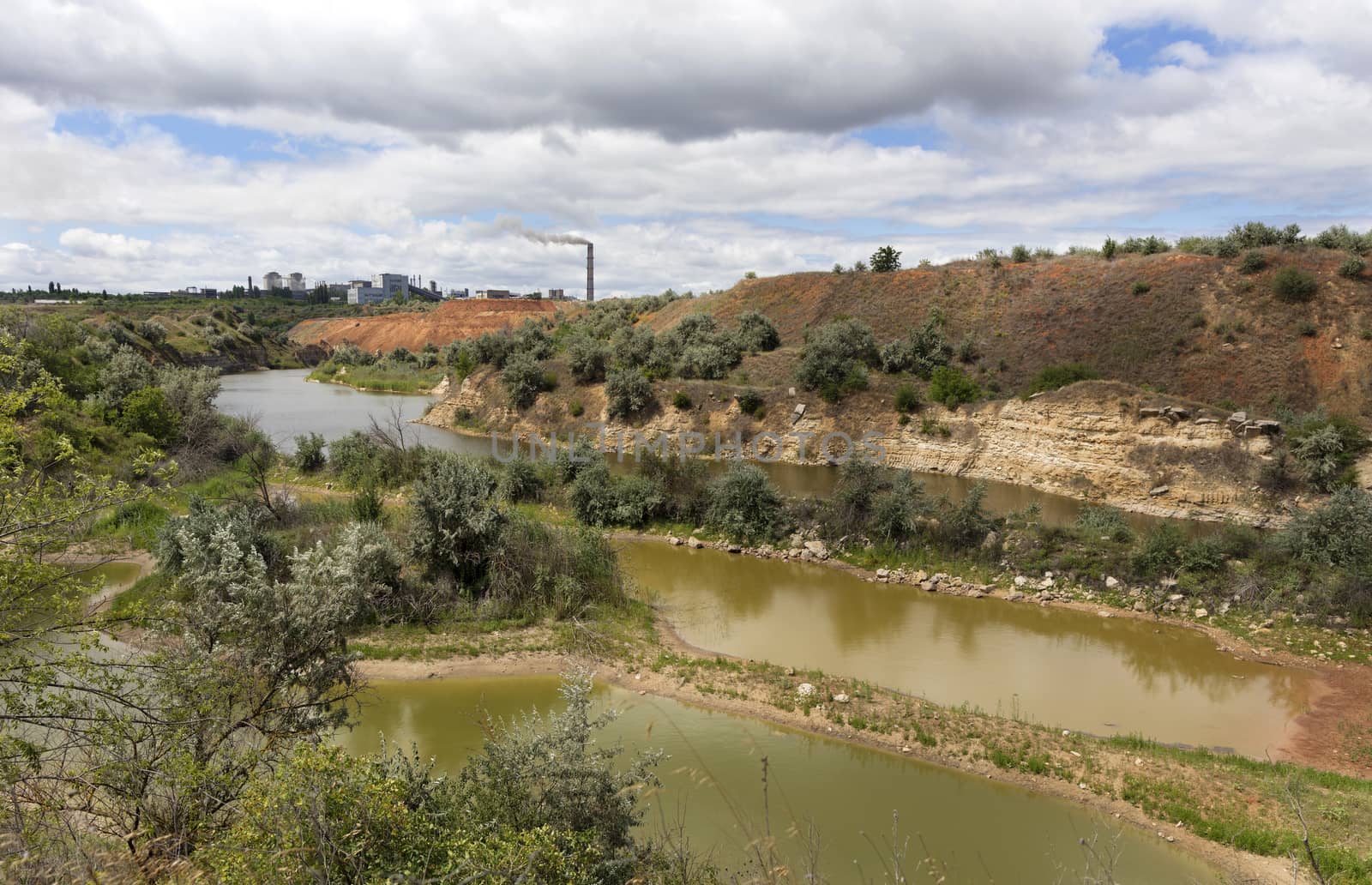 The landscape of an abandoned sandstone quarry on a summer day. Recycling company on the horizon.