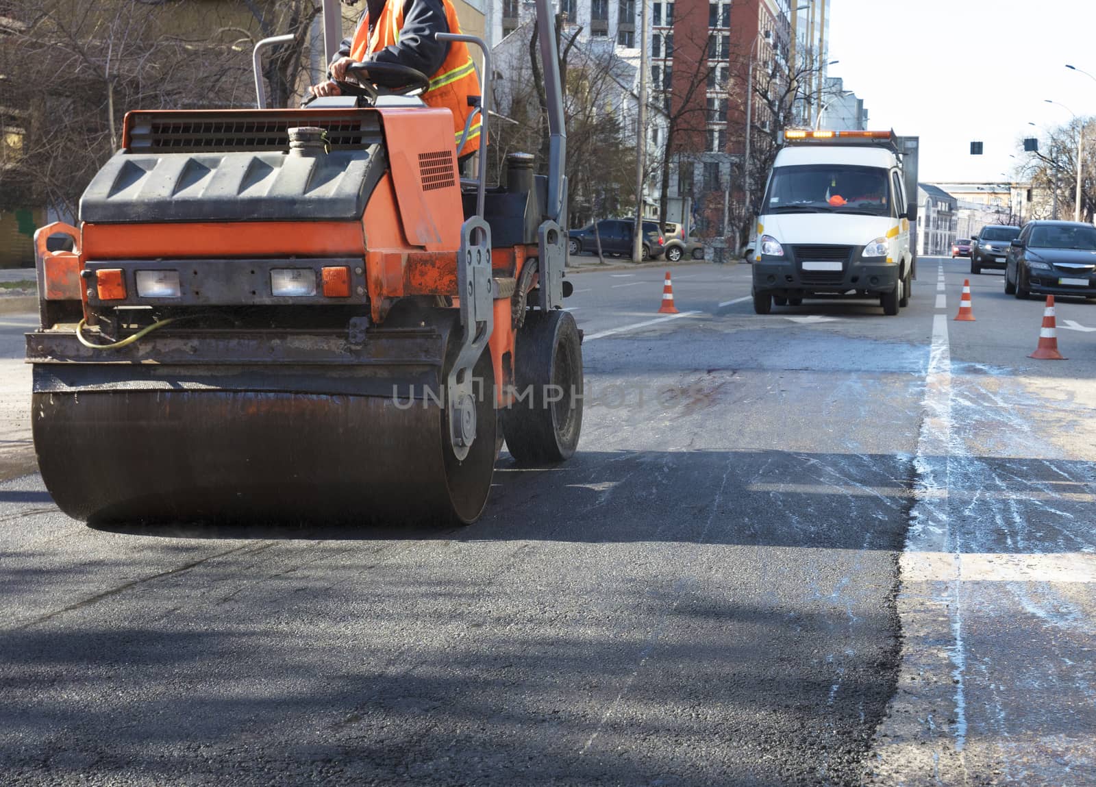 Heavy vibration roller compactor repairs the road on the asphalt surface on the road section of the roadway enclosed by road cones