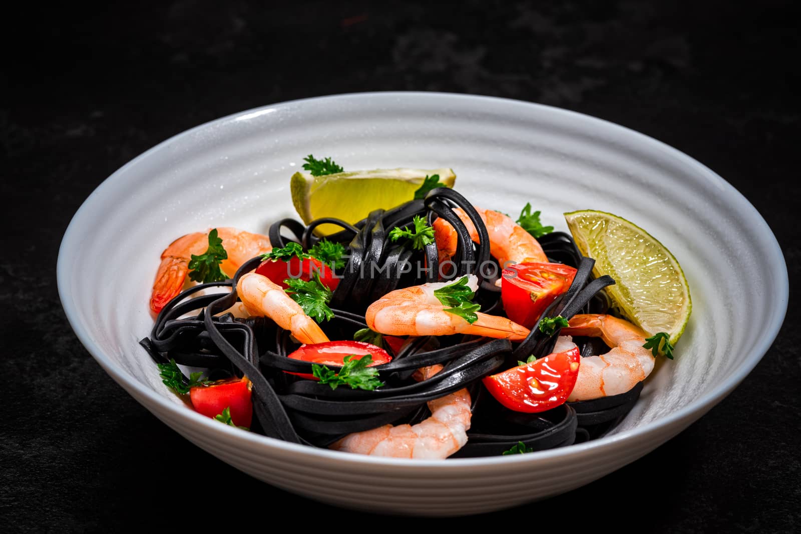 Black Pasta - Squid Ink, with Prawns, Seafood,Lemon and Tomatoes in White Bowl on  Dark Background. Top view.