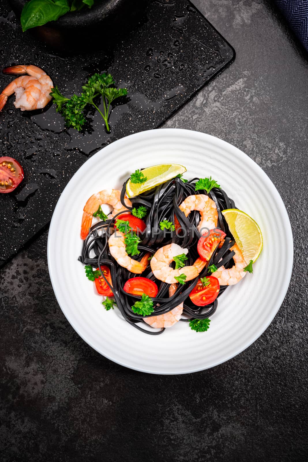 Black Pasta - Squid Ink, with Prawns, Seafood,Lemon and Tomatoes in White Bowl on  Dark Background. Top view.