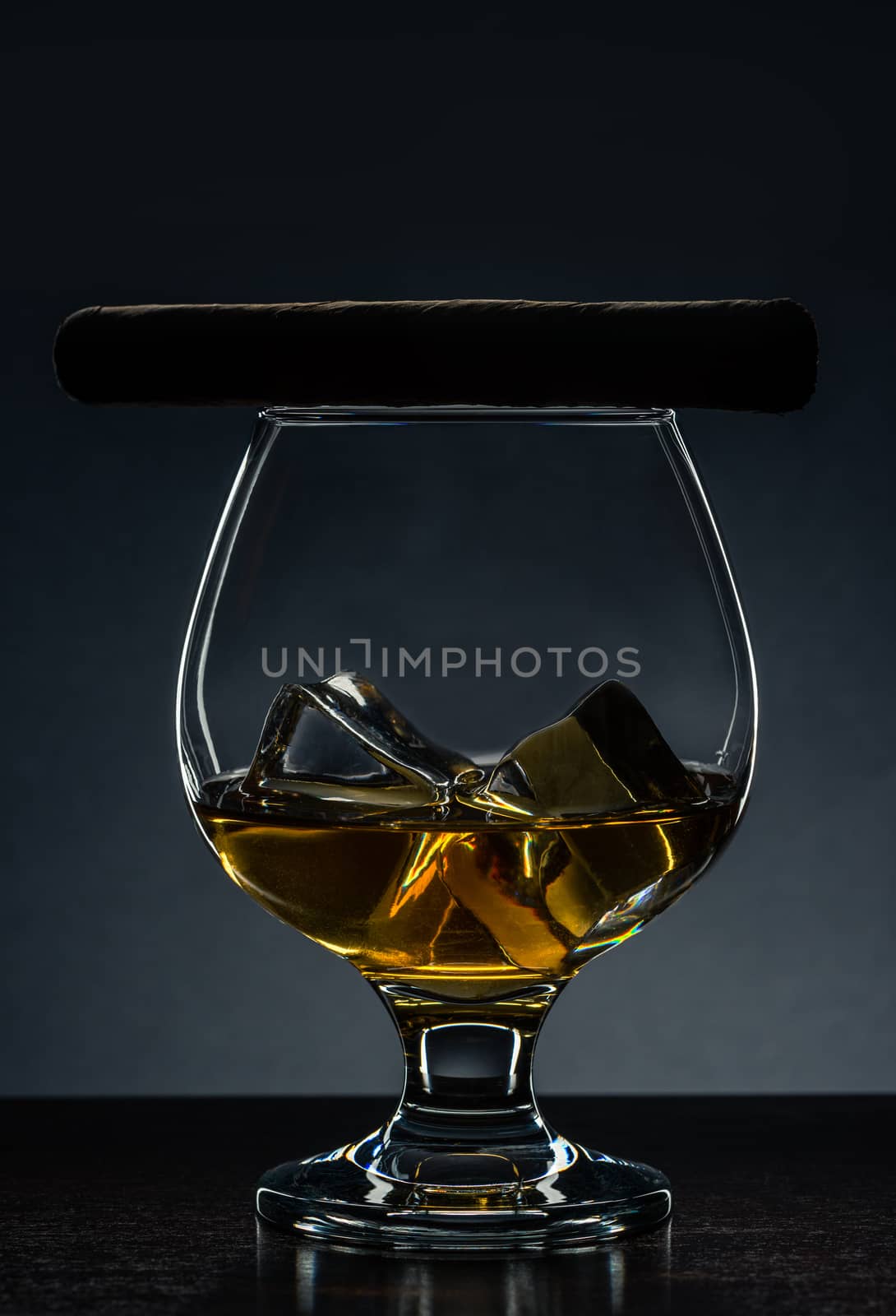 Cuban Cigar on Elegant Glass with Alcohol and Ice Cubes. Luxury Products on Wooden Table.
