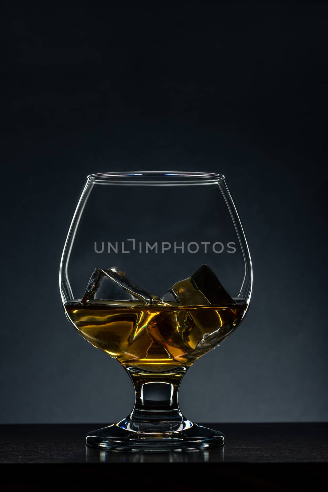 Elegant Glass with Cognac and Ice Cubes on Wooden Table. Copy Space Background.