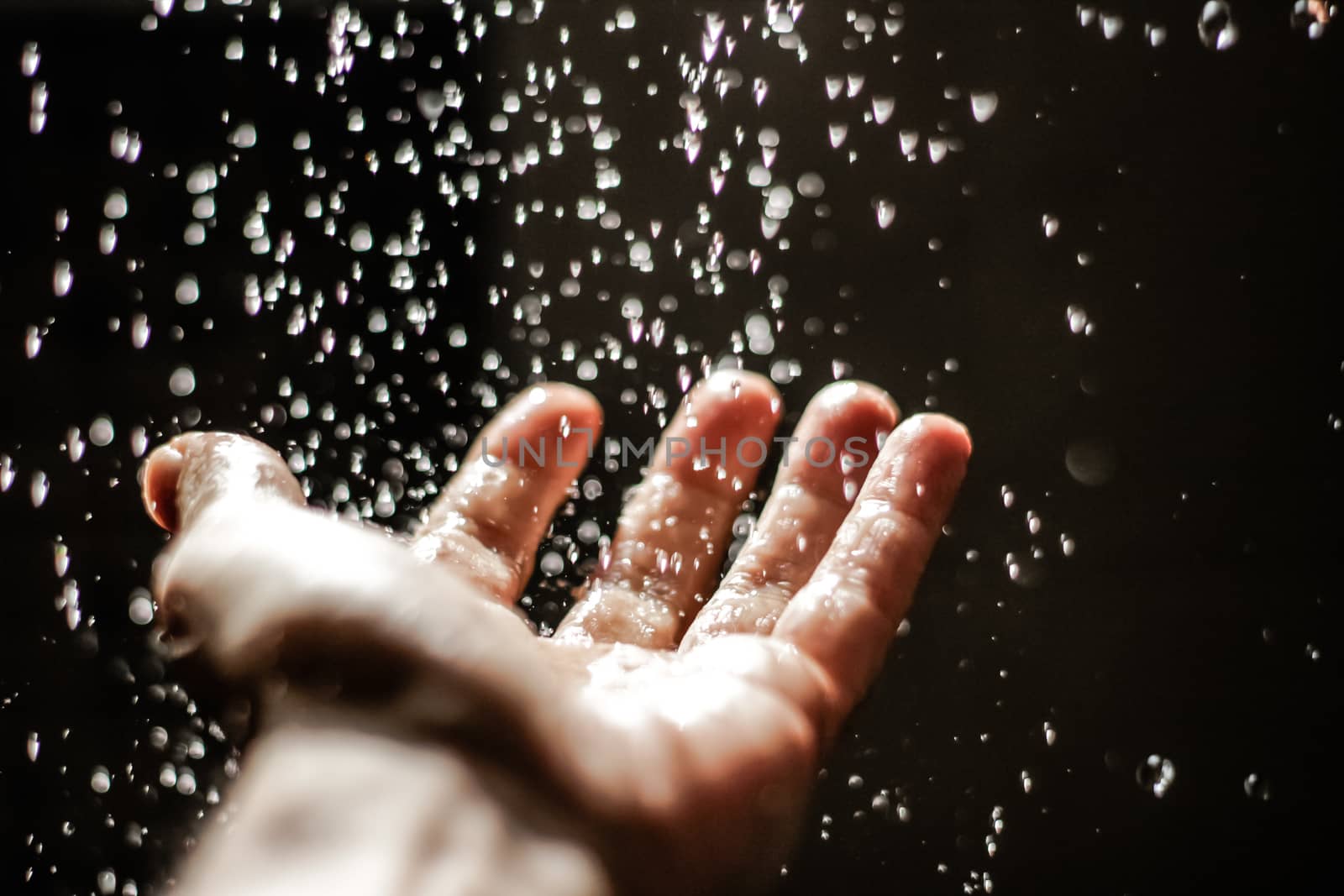 Photograph of an open human hand under water drops