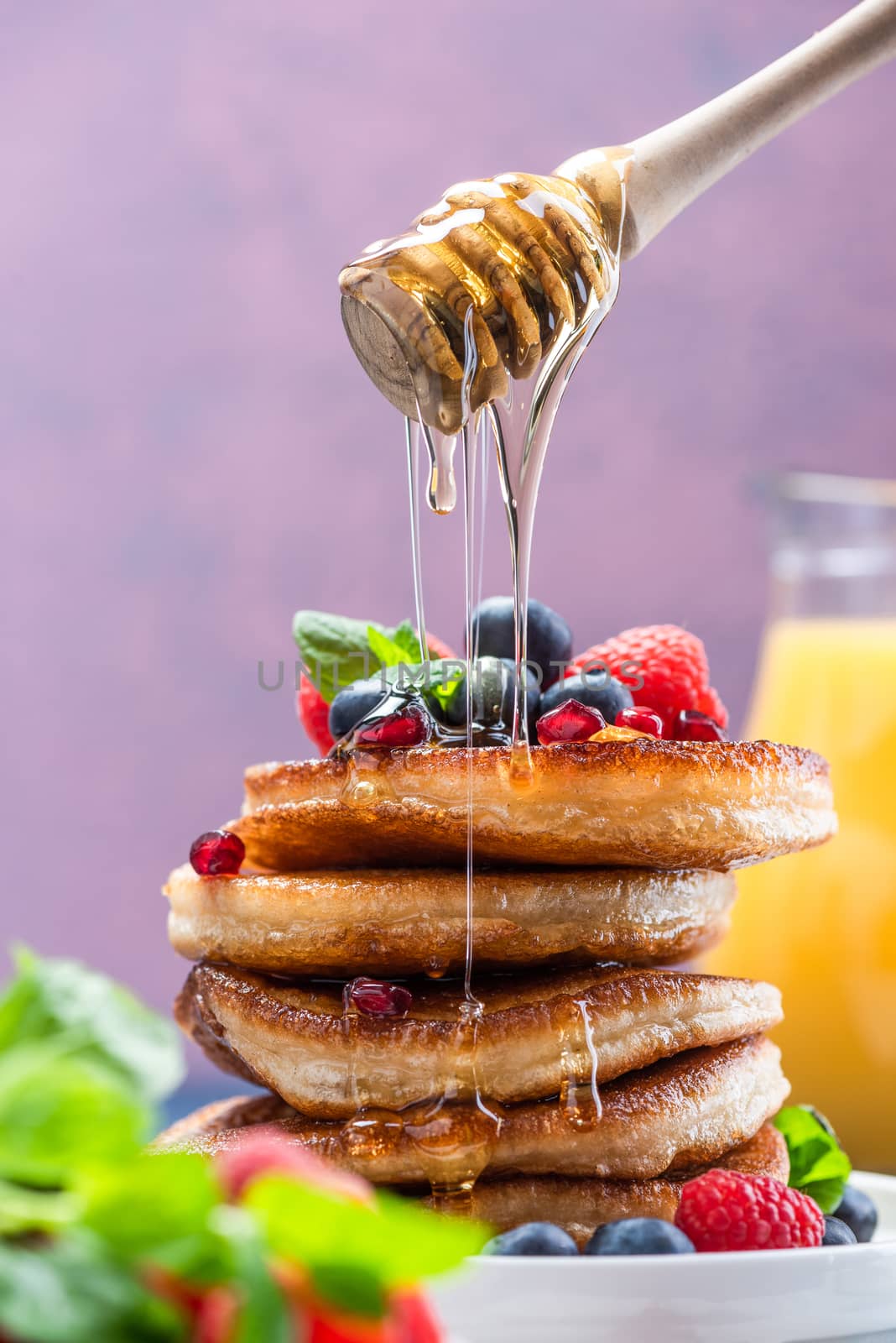 Pouring Honey on Pancakes Stack Topped with fresh Fruits. Shrove Tuesday Breakfast.