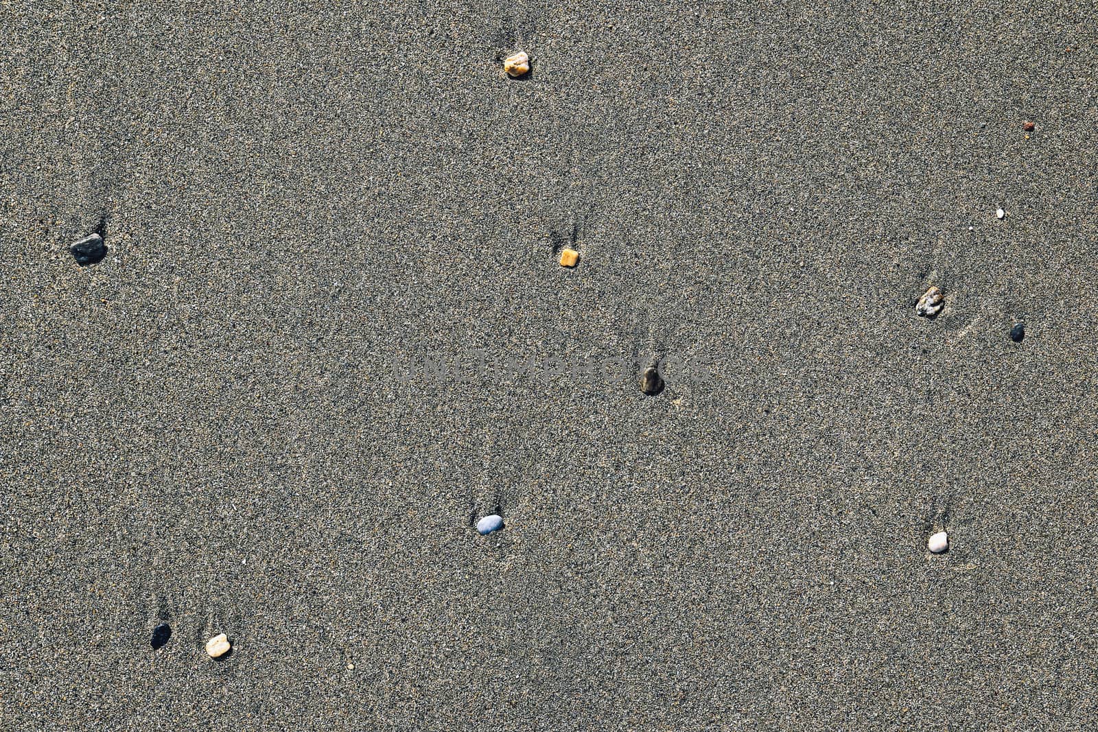 Rare pebble background. Different stones with stains on the wet sand. Beach beauty backdrop.
