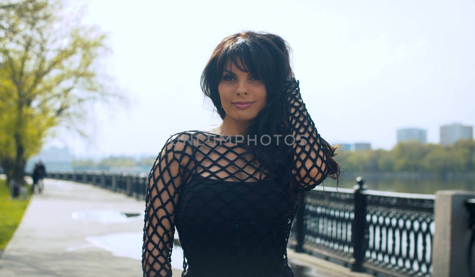 Beautiful smiling woman in black clothes on the embankment in the city park. Nice early spring day. Real people