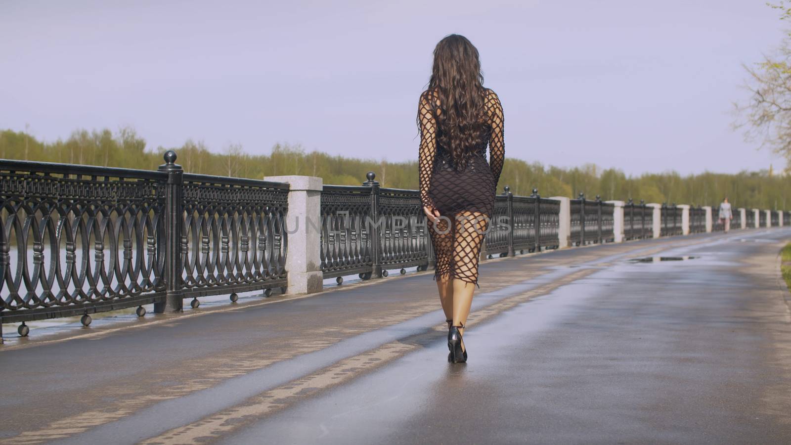 Beautiful fashionably dressed woman walking along the promenade in a city. Nice early spring day, fresh leaves on the trees. Real people. Follow shot