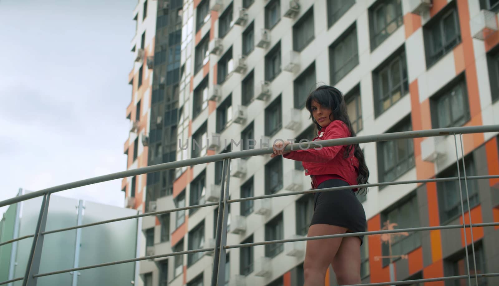 Beautiful woman with long hair standing on a bridge next to a modern building. Low angle view. Real people