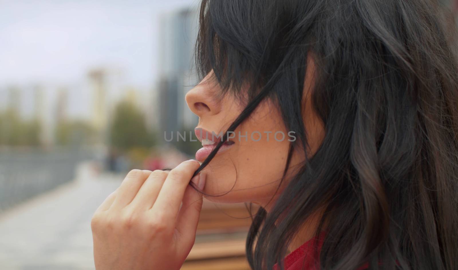 Close up profile portrait of beautiful woman with black long hair outdoors. She plays with a hair. Real people in the city.