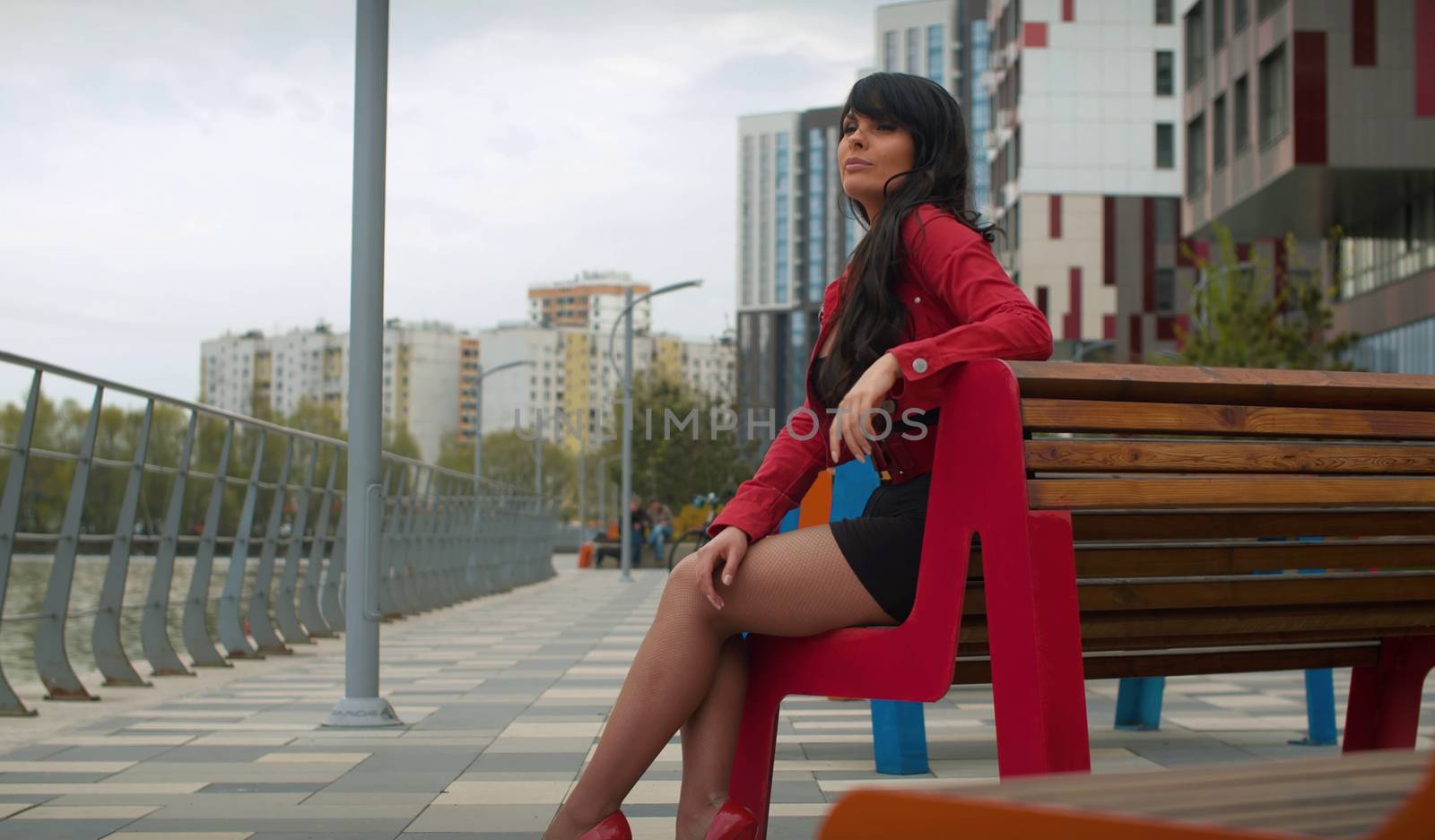 Portrait of beautiful brunette woman with long hair sitting on the bench in the city near the river. Real people.