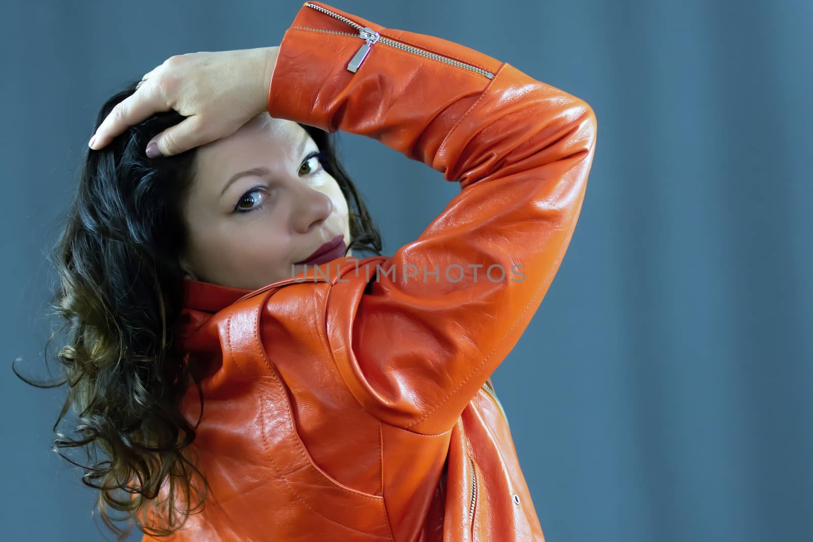 Portrait of a beautiful fashionable middle-aged woman in a bright orange leather jacket, posing on a dark gray background