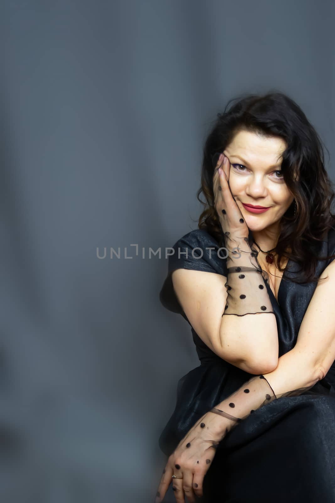 Portrait of a beautiful fashionable middle-aged woman in a bright pink semi-transparent long dress, posing on a dark gray background. The concept of preserving youth at any age.