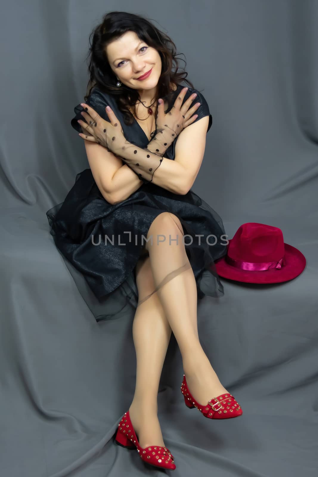 Portrait of a beautiful fashionable middle-aged woman in a bright pink semi-transparent long dress, posing on a dark gray background. by bonilook