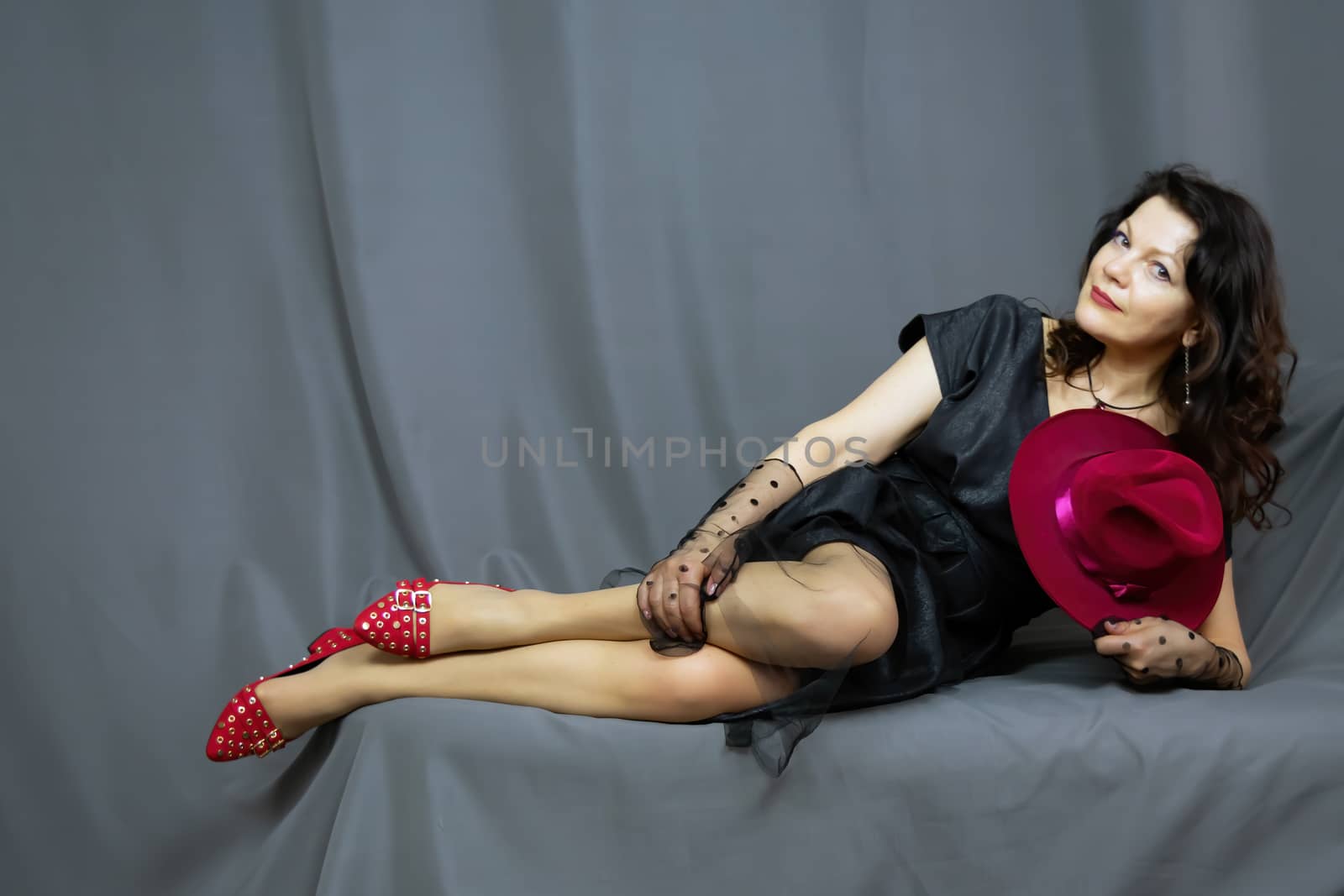 Portrait of a beautiful fashionable middle-aged woman in a bright pink semi-transparent long dress, posing on a dark gray background. The concept of preserving youth at any age.