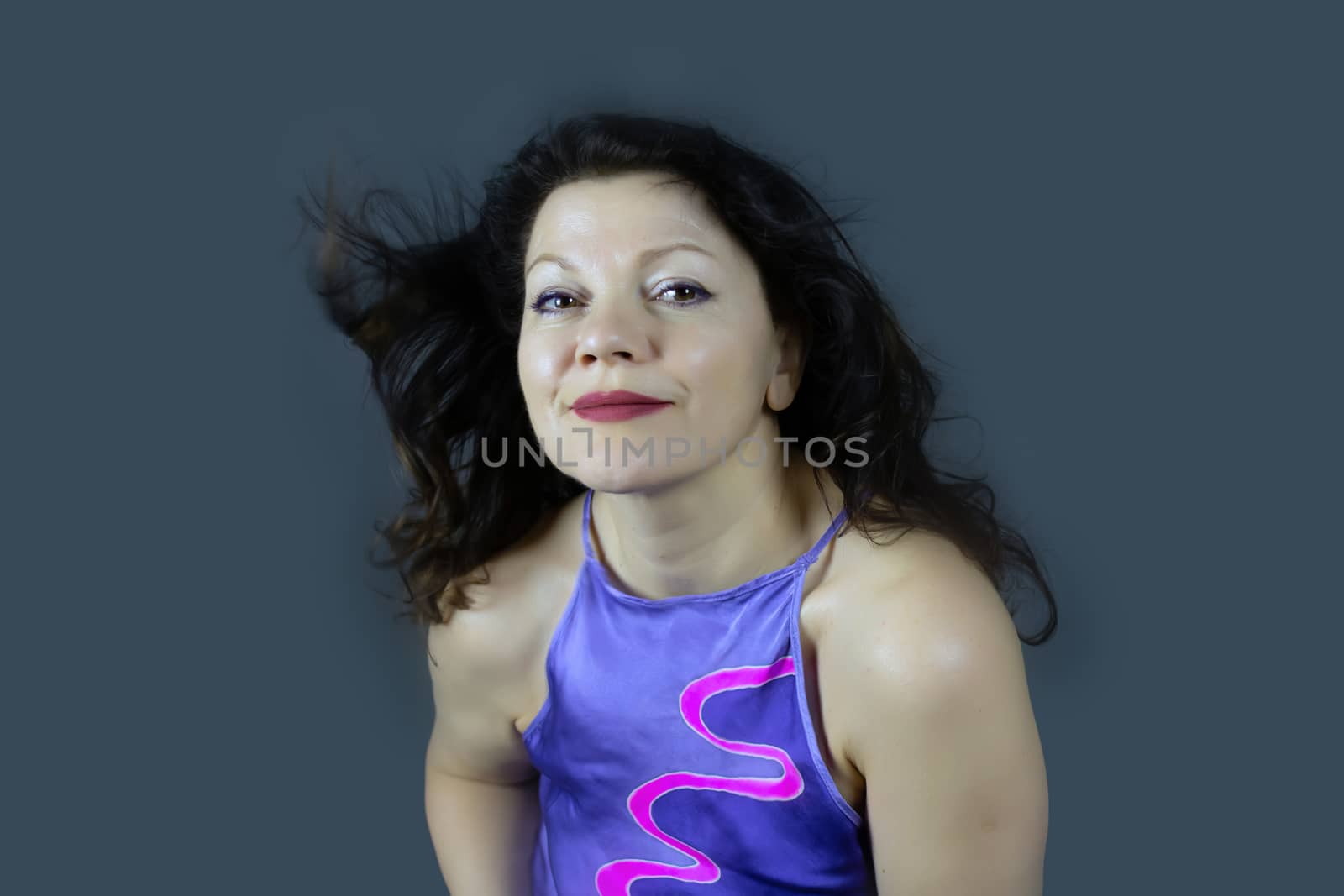 Portrait of a beautiful fashionable middle-aged woman with long dark hair, posing on a dark gray background. The concept of preserving youth at any age.