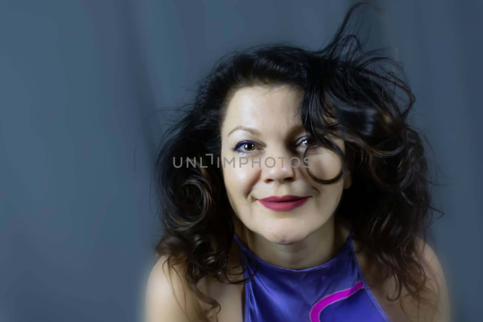 Portrait of a beautiful fashionable middle-aged woman with long dark hair, posing on a dark gray background. The concept of preserving youth at any age.