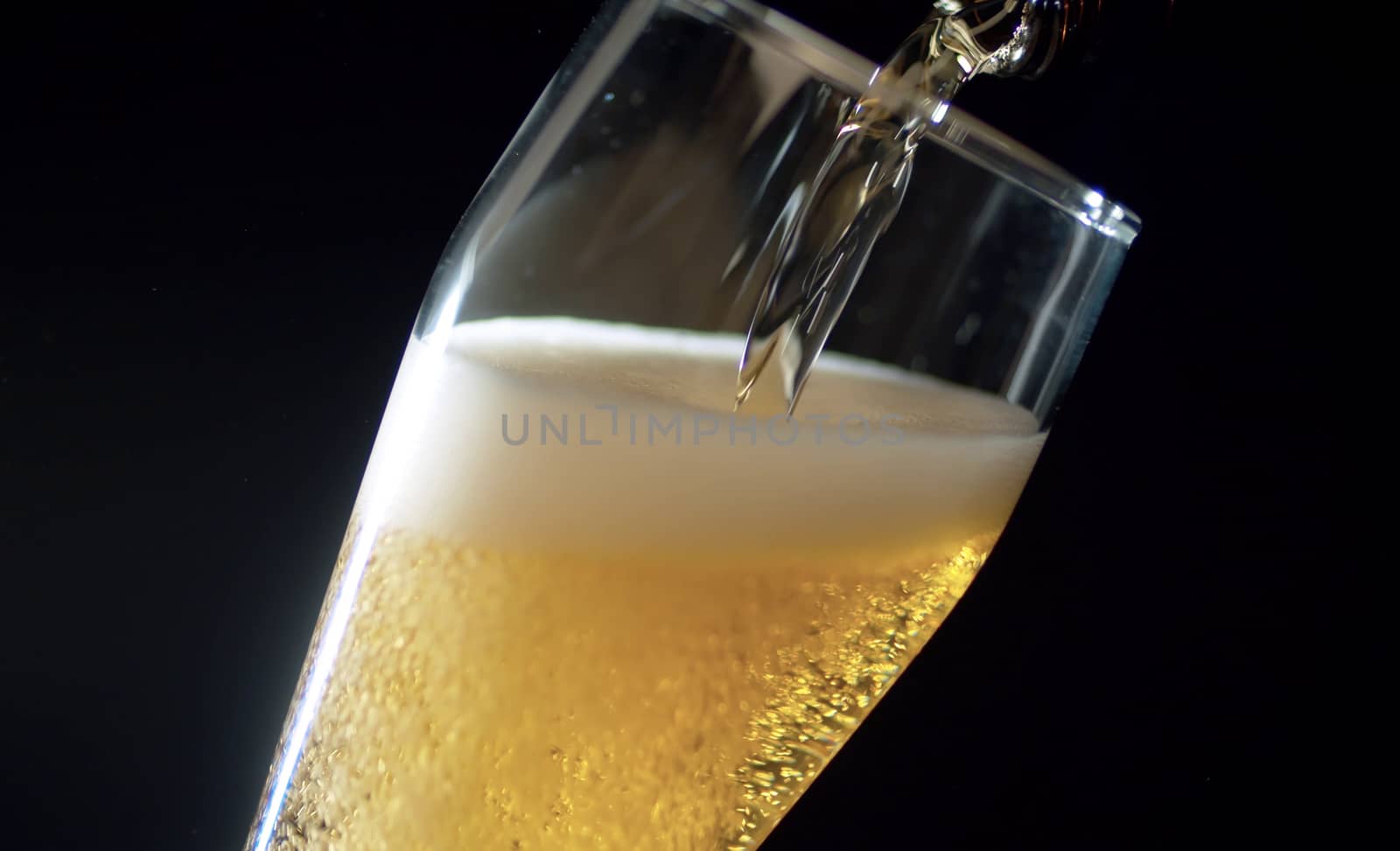 Close up beer pouring into glass on black background. Bubbles rising up and beatifully shining in the light beam.