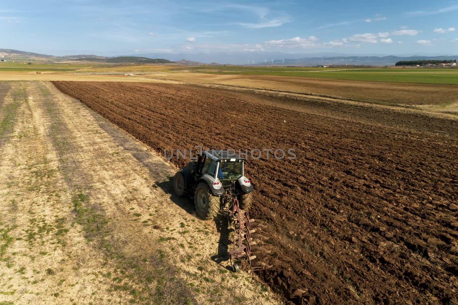 Aerial drone shot of a farmer in tractor seeding, sowing agricultural crops at field in the fertile farm fields of Kilkis in North Greece