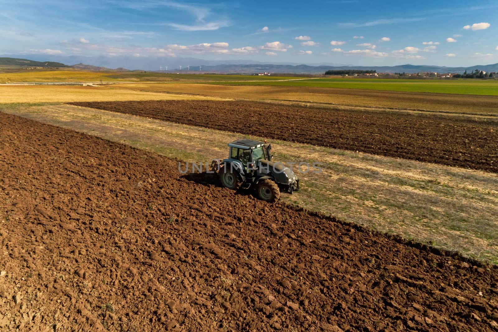 Aerial drone shot of a farmer in tractor seeding, sowing agricultural crops at field in the fertile farm fields of Kilkis in North Greece