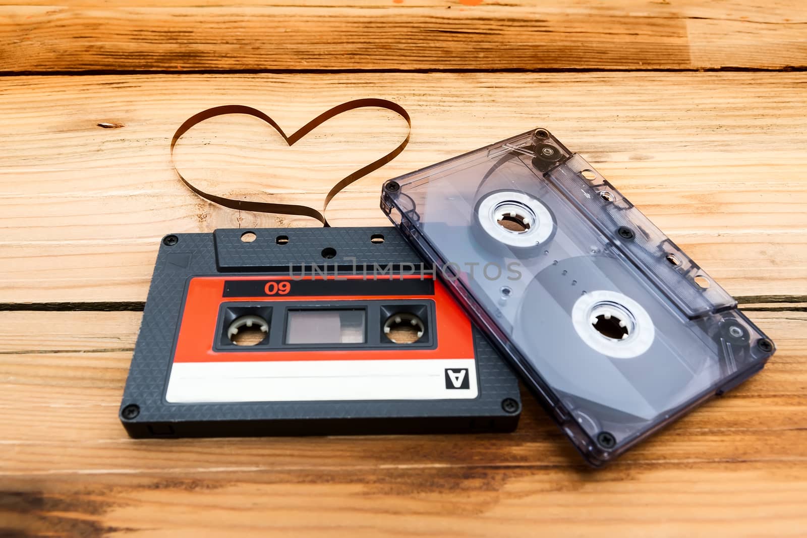 Vintage audio cassette with loose tape shaping one heart on a wooden background.