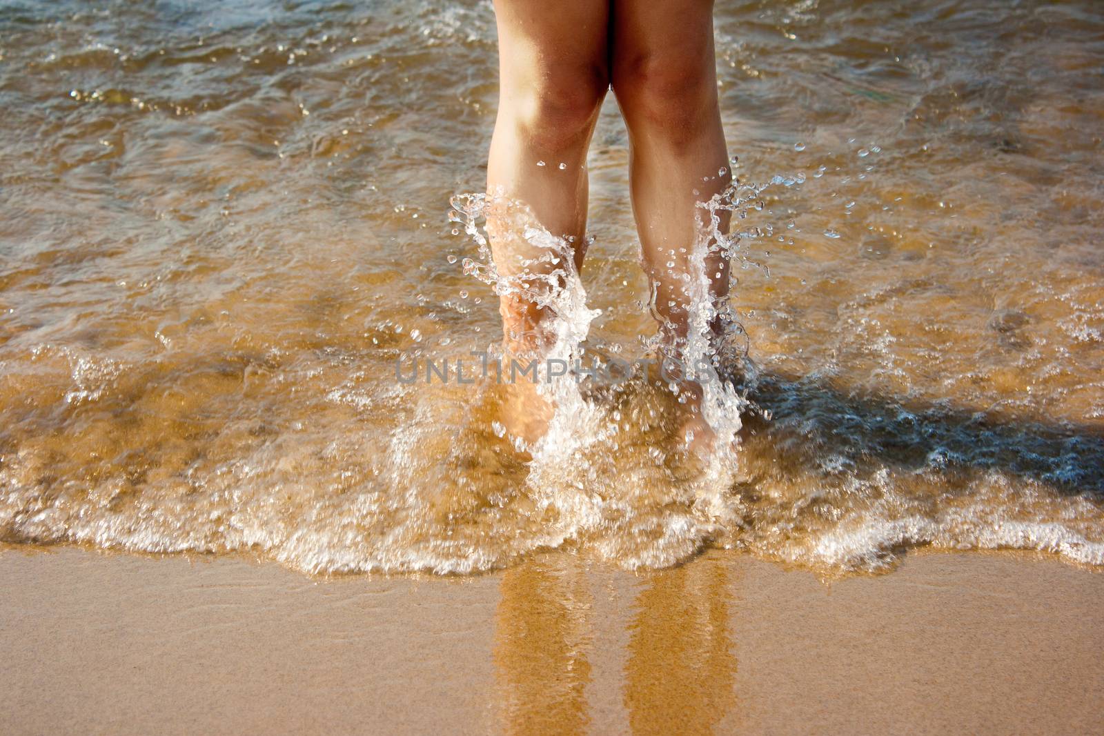 legs of little girl in sea wave on summer closeup
