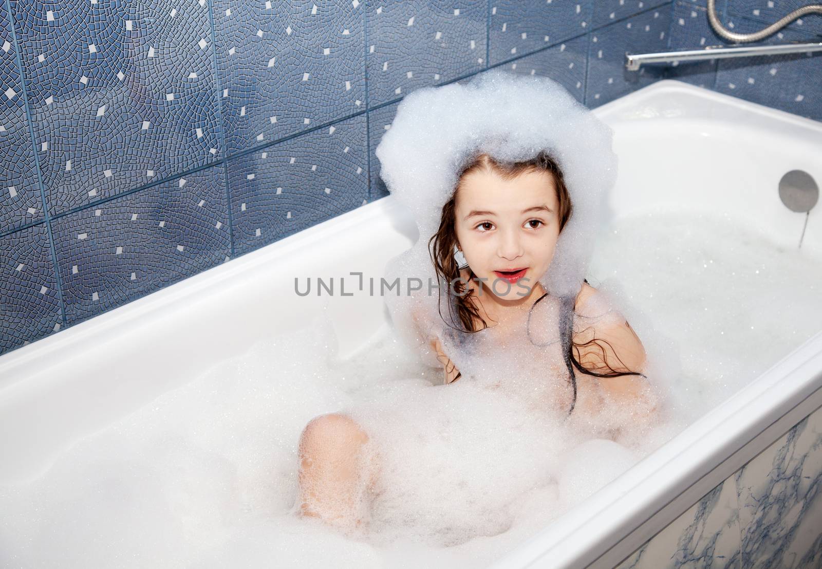 surprised smiling little girl sitting in a bath with soap suds