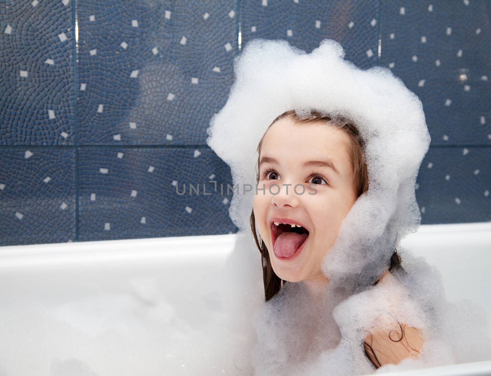 surprised little girl sitting in a bath with soap suds 