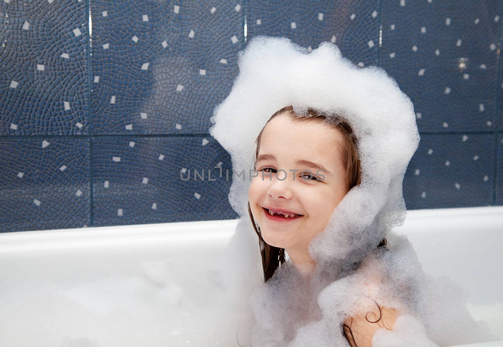 smiling little girl sitting in a bath with soap suds