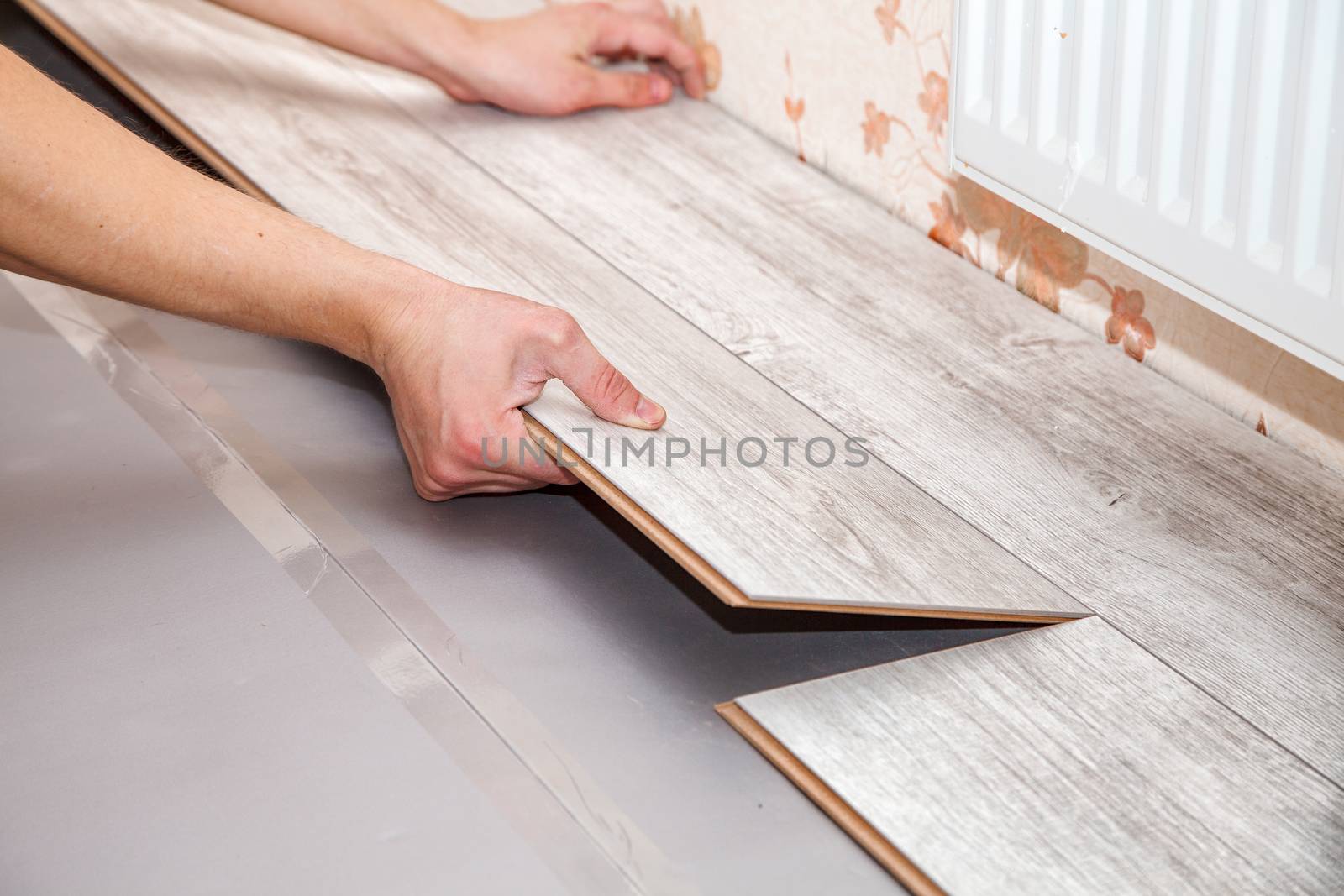 young handyman installing wooden floor in new house, hands closeup